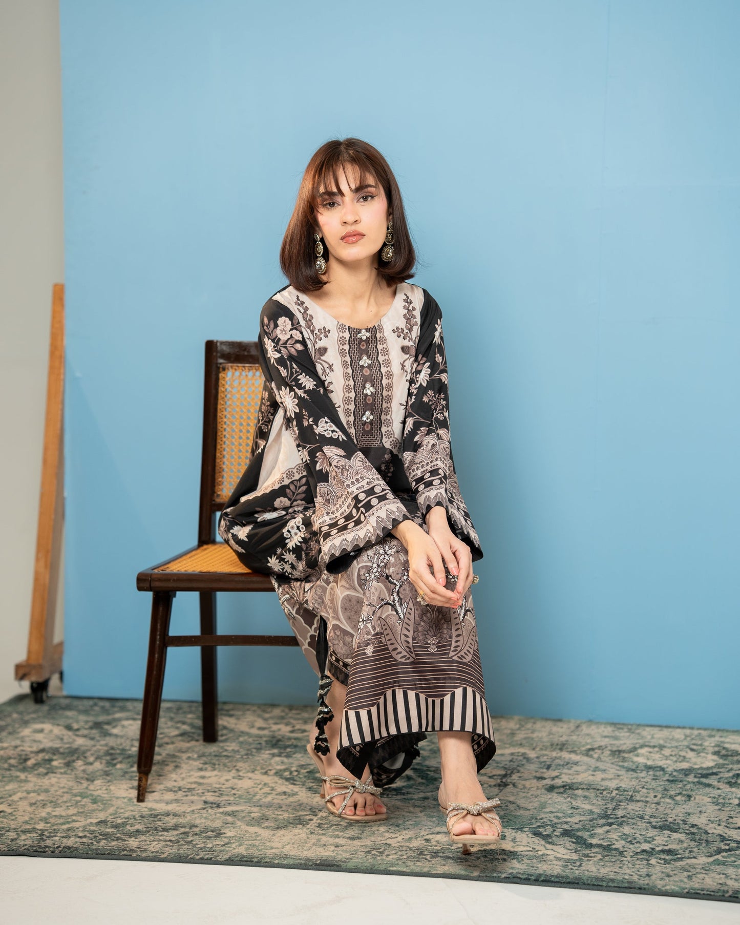 Woman sitting on a chair against a blue wall , Black and ivory floral printed silk kurta wearing, front view SHAFAÉ Midnight Kaftan"