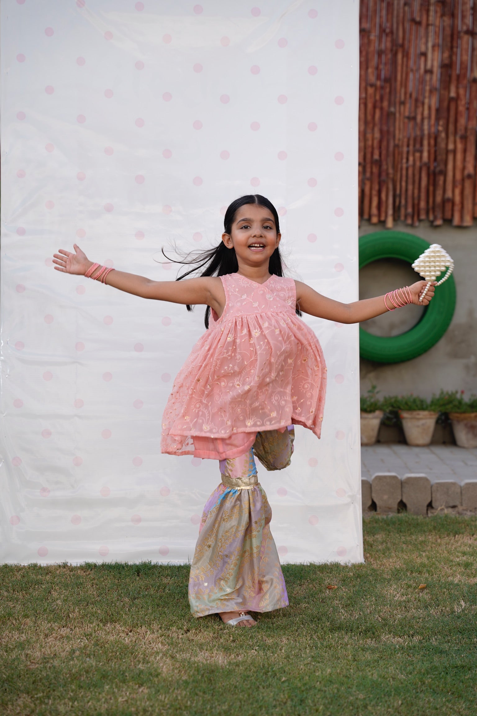 Full front, standing outdoors: "Blush pink embroidered chiffon angrakha top with printed silk gharara, full front view  SHAFAÉ Opal Blush"