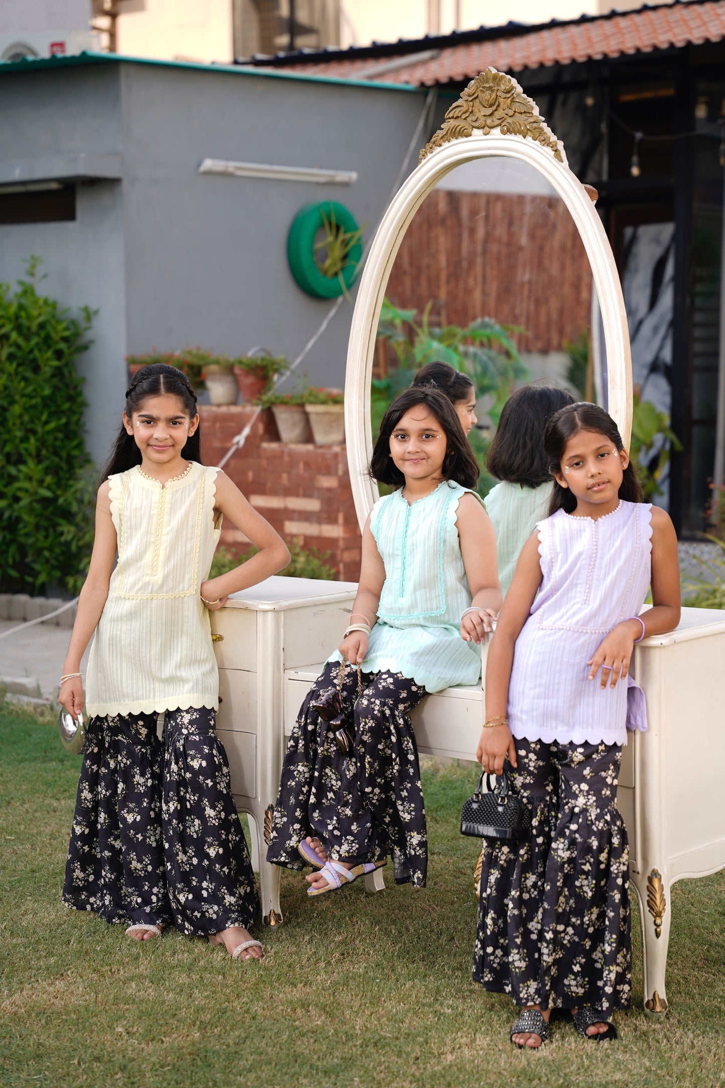 Three young girls in front of a decorative mirror outdoors.