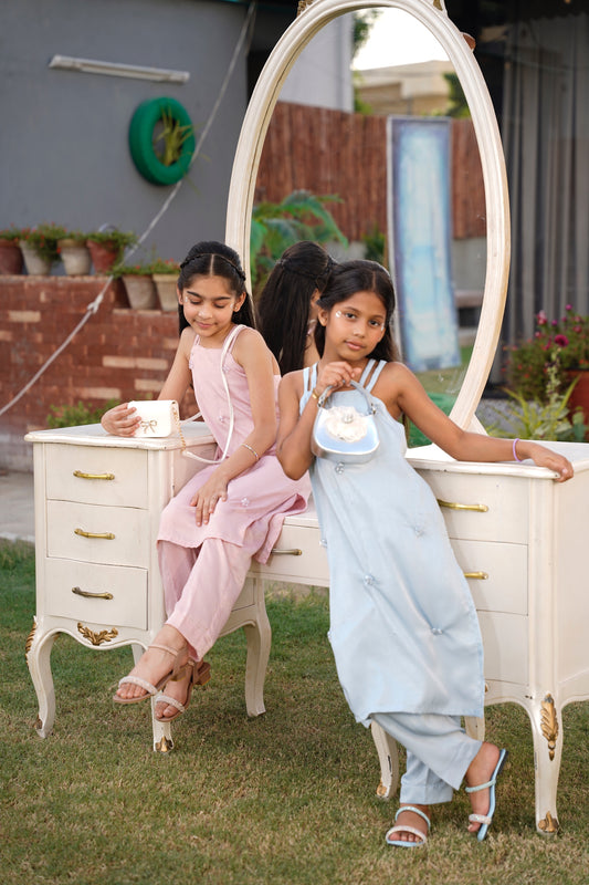 Two young girls sitting on a white vanity with a large mirror outdoors.Full front view: "Blush Sky blue embellished leather silk co-ord set with straight pants, full front view SHAFAÉ Crystal Sky"