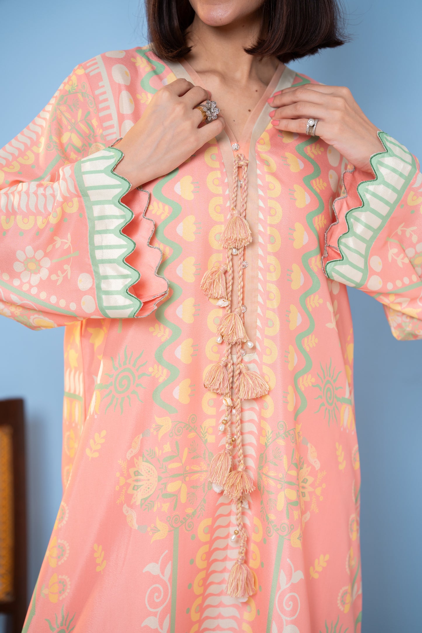  "Close-up of beaded tassel tie on peach printed silk kaftan with cascade sleeves SHAFAÉ Peach Maze"