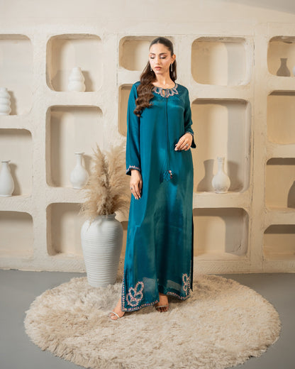 Woman in a teal dress standing in front of a decorative wall with shelves and vases.